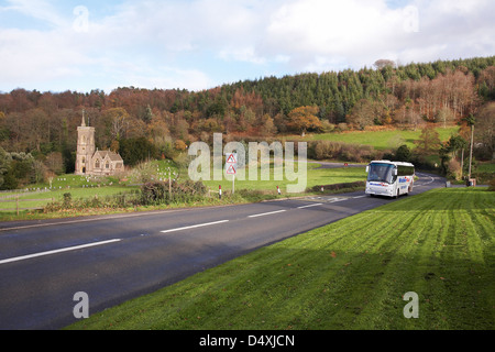 A Webber coach traveling along the A39 at west Quantoxhead, Somerset in England with Saint Etheldreda's Church in the distance Stock Photo