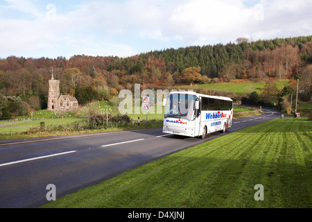 A Webber coach traveling along the A39 at west Quantoxhead, Somerset in England with Saint Etheldreda's Church in the distance. Stock Photo