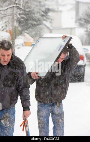 Glaziers carrying a window pane in the snow after their van became stuck on a steep hill, Ambleside, Lake District, UK. Stock Photo