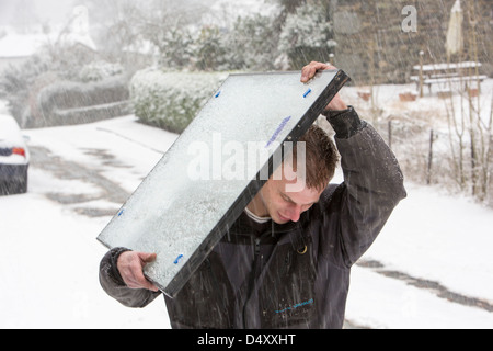 Glaziers carrying a window pane in the snow after their van became stuck on a steep hill, Ambleside, Lake District, UK. Stock Photo