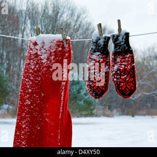 Christmas snow falling vintage red mittens and scarf hanging on a clothesline outdoors winter farm garden, New Jersey, USA, US, colourful laundry Stock Photo