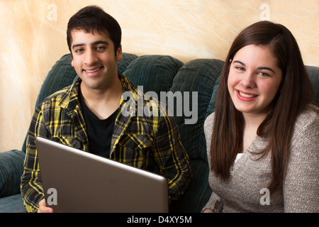A Teenage girl and boy study with a laptop at home on the sofa Stock Photo