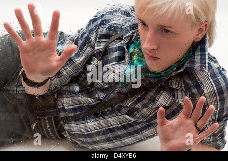 the sad young man leaned hands against wet glass Stock Photo