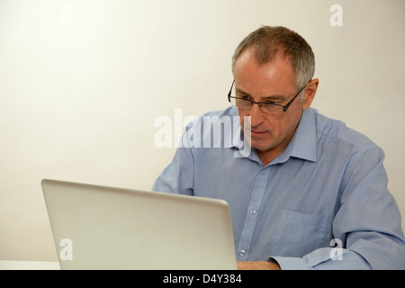 A Caucasian man in his fifties using a laptop. Plain background. Stock Photo