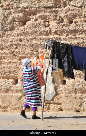 Moroccan housewife hanging out domestic washing on a clothes line within the fortified  city walls of Essaouira, Morocco Stock Photo