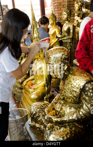 Thailand, Ayutthaya. Wat Phra Chao Phya-thai. Temple visitors place small gold leaf squares on Buddha statues as offering.