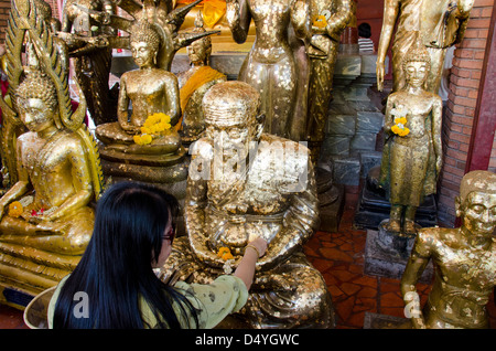 Thailand, Ayutthaya. Wat Phra Chao Phya-thai. Temple visitors place small gold leaf squares on Buddha statues as offering.
