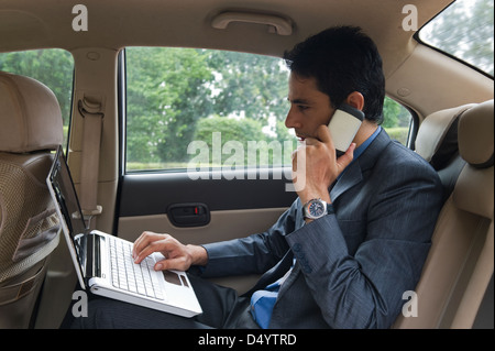 Businessman using a laptop and a mobile phone in a car Stock Photo