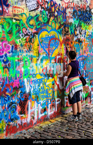 A young tourist girl adds graffiti to the John Lennon Wall in Prague, Praha, Czech Republic,Česká Republika,Europe Stock Photo