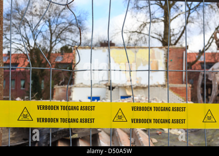Yellow tape with Dutch text 'no trespassing asbestos' on demolition site Stock Photo