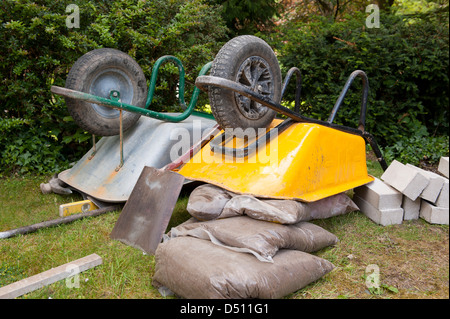 Close-up of building tools & garden landscaping equipment at end of  working day (upturned wheelbarrows, shovel, sand bags) - Yorkshire, England, UK. Stock Photo
