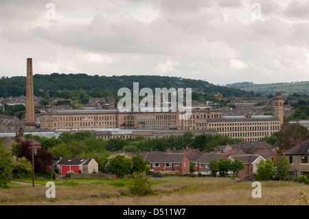 Historic impressive Salts Mill (Victorian textile mill) in Aire valley, tall chimney & weaving sheds towering over houses - Saltaire, England, GB, UK. Stock Photo