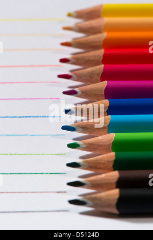 Close-up detail of sharp colourful pencil crayons laid side by side on white paper background by lines drawn in each colour - Yorkshire, England, UK. Stock Photo
