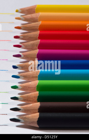 Close-up detail of sharp colourful pencil crayons laid side by side on white paper background by lines drawn in each colour - Yorkshire, England, UK. Stock Photo