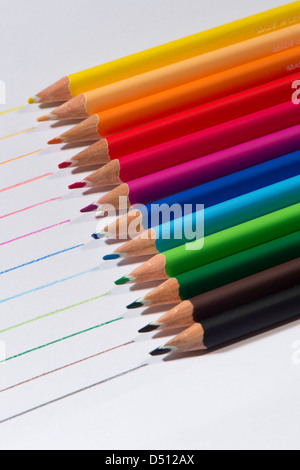 Close-up detail of sharp colourful pencil crayons laid side by side on white paper background by lines drawn in each colour - Yorkshire, England, UK. Stock Photo