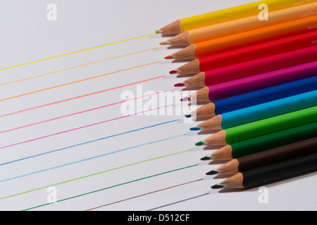 Close-up detail of sharp colourful pencil crayons laid side by side on white paper background by lines drawn in each colour - Yorkshire, England, UK. Stock Photo