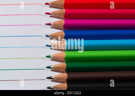 Close-up detail of sharp colourful pencil crayons laid side by side on white paper background by lines drawn in each colour - Yorkshire, England, UK. Stock Photo