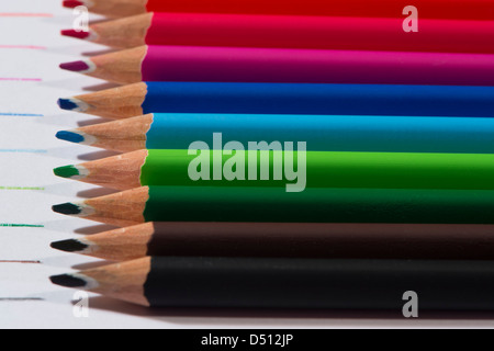 Close-up detail of sharp colourful pencil crayons laid side by side on white paper background by lines drawn in each colour - Yorkshire, England, UK. Stock Photo