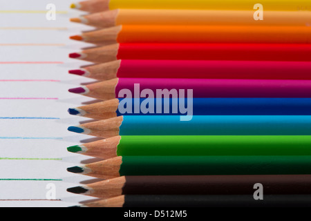 Close-up detail of sharp colourful pencil crayons laid side by side on white paper background by lines drawn in each colour - Yorkshire, England, UK. Stock Photo
