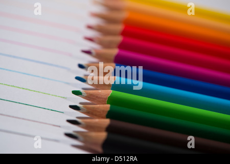 Close-up detail of sharp colourful pencil crayons laid side by side on white paper background by lines drawn in each colour - Yorkshire, England, UK. Stock Photo
