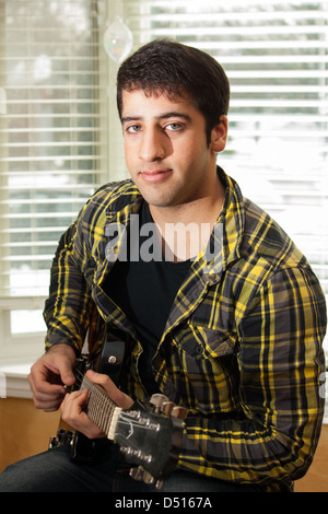 An attractive teenage boy looks at the camera while playing an electric guitar Stock Photo