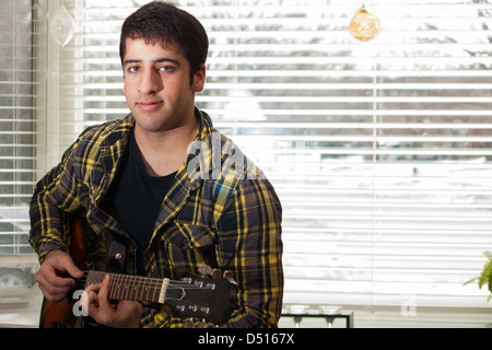 An attractive teenage boy looks at the camera while playing an electric guitar Stock Photo