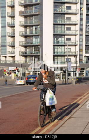 A cyclist breaking the law by using mobile phone whilst steering with one hand and a bag draped over handlebars. Stock Photo