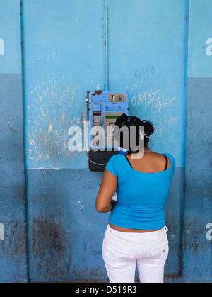 Woman in blue talking on pay phone of similar color with blue wall of same color as woman's blouse in Havana, Cuba Stock Photo