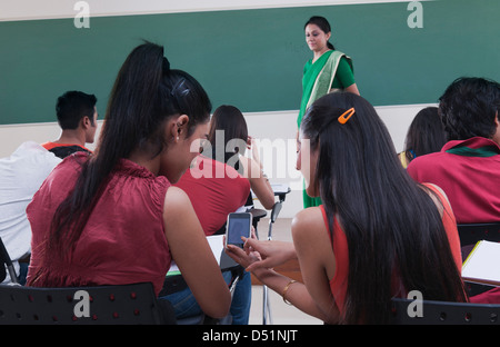 Friends reading messages on a mobile phone in a classroom Stock Photo