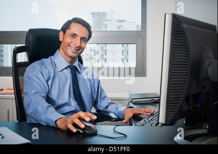Businessman working on a computer in his office and smiling Stock Photo