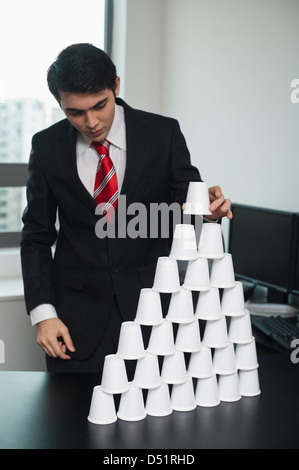 Businessman making a pyramid with disposable cups Stock Photo