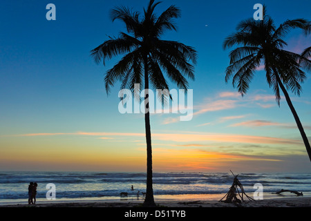 Romantic couple by palm trees on Playa Guiones surf beach at sunset, Nosara, Nicoya Peninsula, Guanacaste Province, Costa Rica Stock Photo