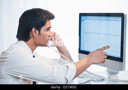 Businessman looking at a computer while talking on a landline phone Stock Photo