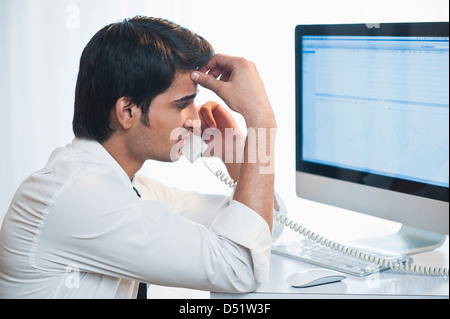 Businessman looking at a computer while talking on a landline phone Stock Photo