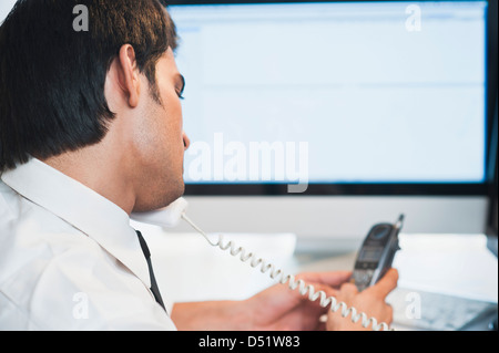 Businessman talking on a landline phone while using a cordless phone Stock Photo