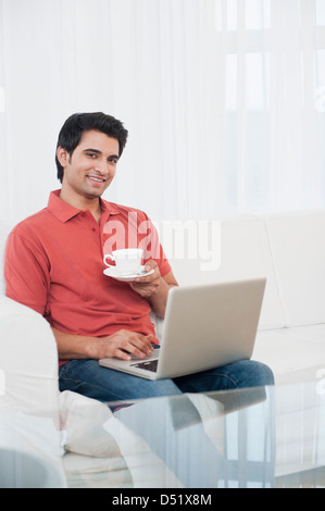 Happy man using a laptop while drinking coffee Stock Photo