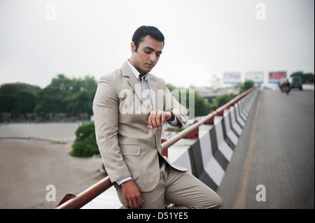 Businessman leaning against flyover railing and checking the time Stock Photo