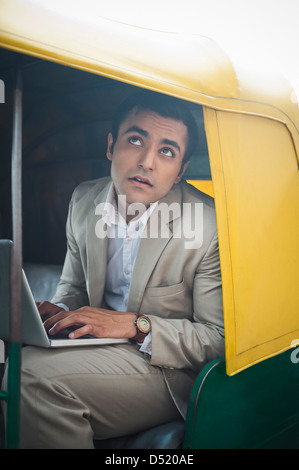 Businessman using laptop while traveling in an auto rickshaw Stock Photo
