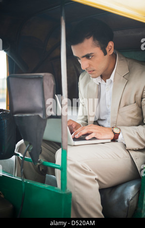 Businessman using laptop while traveling in an auto rickshaw Stock Photo