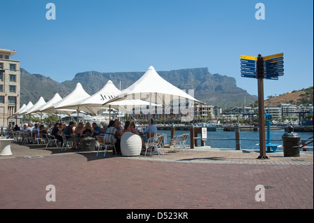 V&A Waterfront Cape Town & Table Mountain. Tourists at cafe tables overlook the harbour South Africa Stock Photo