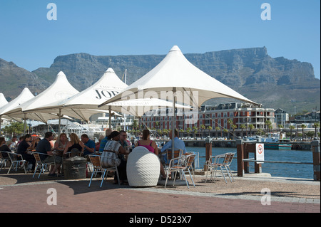 V&A Waterfront Cape Town & Table Mountain. Tourists at cafe tables overlook the harbour South Africa Stock Photo