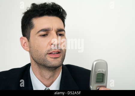 Mid-adult businessman looking at cell phone, frowning Stock Photo