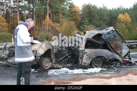 A policemen examines burnt-out vehicles after a severe car crash south of Berlin in Beelitz, Germany, 30 October 2010. Four people died in the accident that involved three cars and three trucks on Autobahn 9. Photo: NESTOR BACHMANN Stock Photo