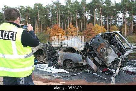 A policeman takes pictures of burnt-out vehicles after a severe car crash south of Berlin in Beelitz, Germany, 30 October 2010. Four people died in the accident that involved three cars and three trucks on Autobahn 9. Photo: NESTOR BACHMANN Stock Photo