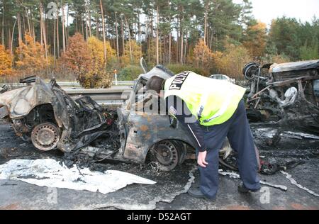 A policeman examines burnt-out vehicles after a severe car crash south of Berlin in Beelitz, Germany, 30 October 2010. Four people died in the accident that involved three cars and three trucks on Autobahn 9. Photo: NESTOR BACHMANN Stock Photo