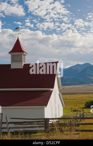 An old mountain ranch sits in the middle of hay meadows and fields, with the Sangre de Cristo Mountain Range in the background. Stock Photo