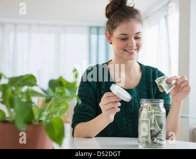 Hispanic girl putting money in savings jar Stock Photo