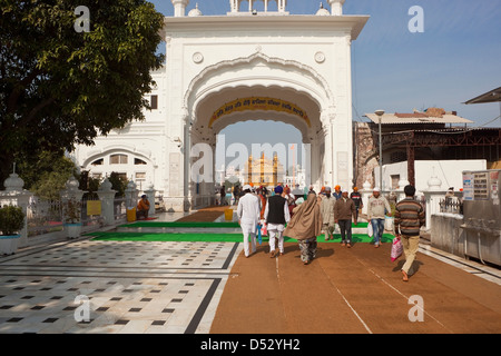 A busy scene inside the Golden Temple complex with temple guard, pilgrims and trees on a sunny day in Amritsar Punjab Stock Photo