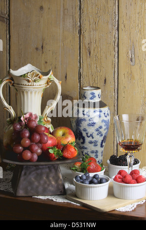 a still life photo of fruits, berries, vases and wine glass Stock Photo
