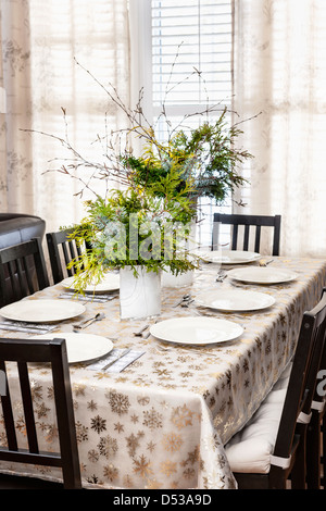 Dining table decorated for Christmas with eight place settings and evergreen centerpiece Stock Photo